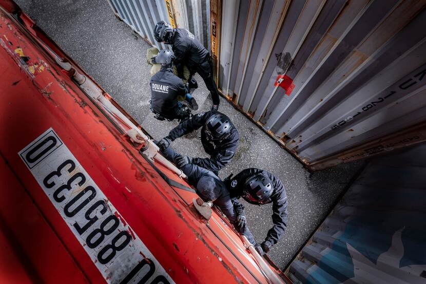 douaniers met bivakmutsen op doen een aanhouding tussen de containers